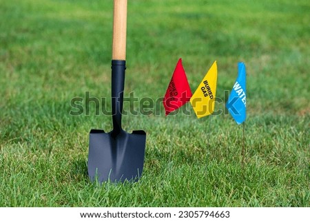Buried electric, natural gas and water utility warning flag with shovel. Notify utility locate company for underground utilities, call before you dig and digging safety concept Royalty-Free Stock Photo #2305794663