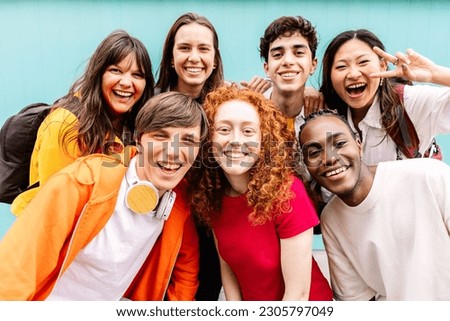 Diverse group of teenage student friends standing together over blue background. Portrait of young multiracial college people team having fun smiling at camera. Youth community and friendship concept