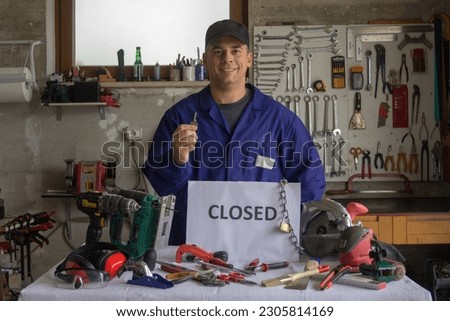 Image of a smiling handyman in his workshop with an CLOSED sign and various work tools. Reopening of work activities and work development
