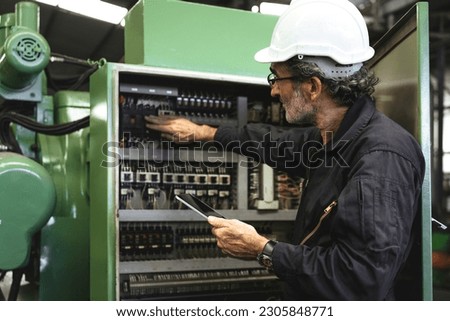 Electrical Engineer team working front control panel, An electrical engineer is installing and using a tablet to monitor the operation of an electrical control panel in a factory service room. Royalty-Free Stock Photo #2305848771