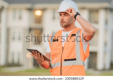 Engineer with tablet, building inspection. Builder at construction site. Buider with helmet on construction outdoor. Worker at construction site. Bilder in hardhat. Royalty-Free Stock Photo #2305880129