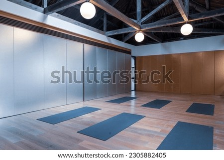 Elegant fitness gym interior with exercise mat and wooden roof, ball and dumbbell. White wall, oak wooden floor, panoramic window. Concept of place for yoga, gymnastics, training, meditating.