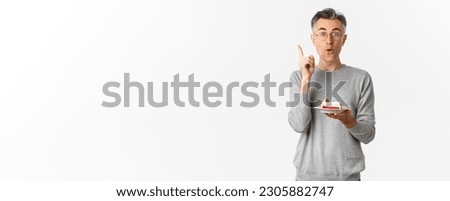 Image of happy middle-aged man, celebrating birthday, have great idea what to wish while blowing candle on b-day cake, standing over white background.
