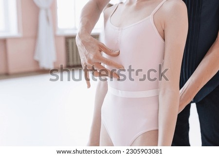 The trainer points to the little ballerina's diaphragm with his hands. She an aspiring ballet dancer. rearview shot of a little girl practicing ballet in a dance studio. Royalty-Free Stock Photo #2305903081