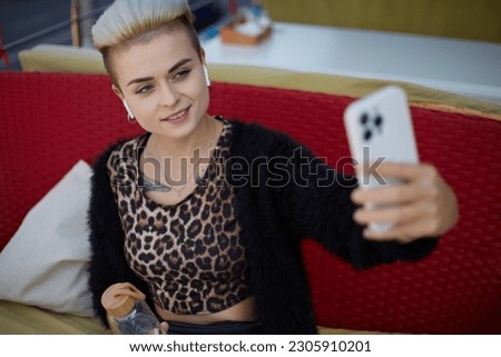 Beautiful tom boy woman with short hair taking a seflie photo in a restaurant. Cheerful diverse female in leopard clothes posing for a photo in a cafe