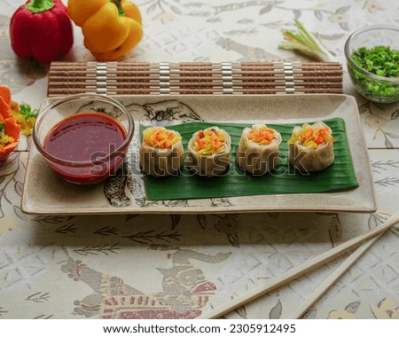 Chicken Sui mui dim sums in a ceramic plate with sauce, bell papers, chopsticks on side.