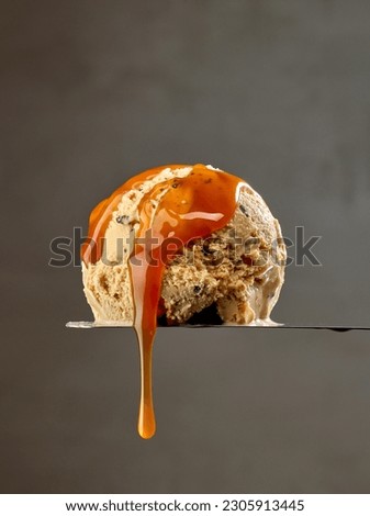 ice cream scoop with flowing melted caramel sauce drop on dark grey wall background Royalty-Free Stock Photo #2305913445