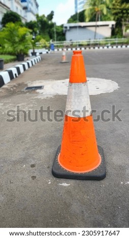 A plastic orange traffic parking cone is on the side of the road