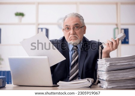 Old male employee speaking by phone in the office Royalty-Free Stock Photo #2305919067