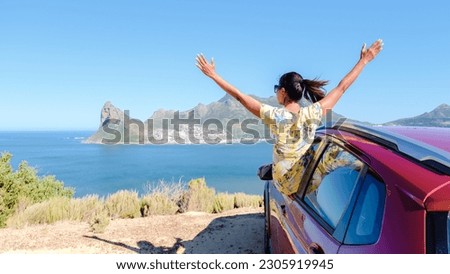 woman outside a car window with hands up, a car at Chapmans Peak Drive in Cape Town South Africa looking out over the ocean. women on a road trip garden route South Africa with renal car Royalty-Free Stock Photo #2305919945