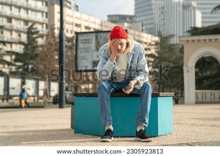 Depressed desperated guy hipster with phone sitting on bench in city having problems troubles. Frustrated confused man has bad news reads message on smartphone. Unfavorable life circumstances concept. Royalty-Free Stock Photo #2305923813