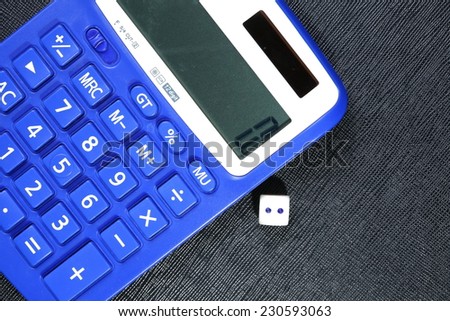 Close up photo of blue color calculator and dice on black leather surface background focusing on calculator button