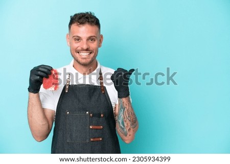 Butcher caucasian man wearing an apron and serving fresh cut meat isolated on blue background pointing to the side to present a product