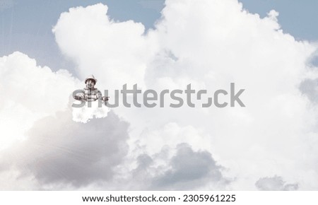 Young little boy keeping eyes closed and looking concentrated while meditating on clouds in the air with cloudy skyscape on background.