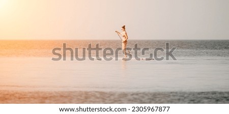 Sea woman sup. Silhouette of happy middle aged tanned woman in rainbow bikini, surfing on SUP board, confident paddling through water surface. Idyllic sunset. Active lifestyle at sea or river.