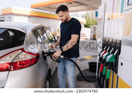 Handsome young man refueling car at gas station. Male filling diesel at gasoline fuel in car using a fuel nozzle. Petrol concept. Side view Royalty-Free Stock Photo #2305974785