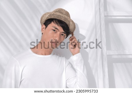 young man wearing white shirt ,straw hat with palm shadow  posing  in studio Royalty-Free Stock Photo #2305995733