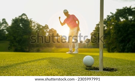 Blurred golfer putting ball on the green golf, lens flare on sun set evening time. Golfer action to win after long putting golf ball in to the hole.                                 