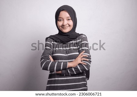Cheerful beautiful Asian muslim woman in brown sweater crossing hands and smiling at camera isolated over white background
