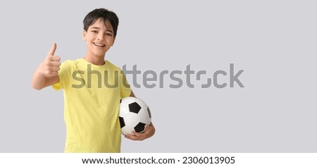 Little boy with soccer ball showing thumb-up on grey background with space for text