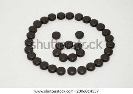 Black pills arranged in a happy smiley on white background.