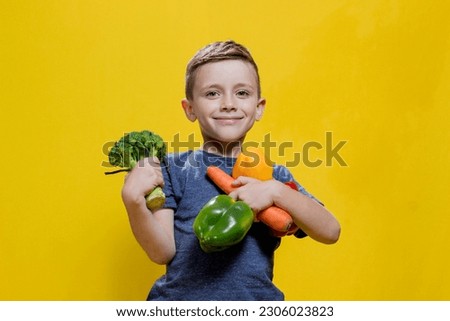 The boy holds fresh vegetables in his hands: broccoli, carrots and peppers on a yellow background. Vegan and healthy concepts Royalty-Free Stock Photo #2306023823