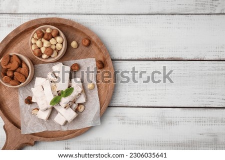 Pieces of delicious nutty nougat on white wooden table, top view. Space for text Royalty-Free Stock Photo #2306035641