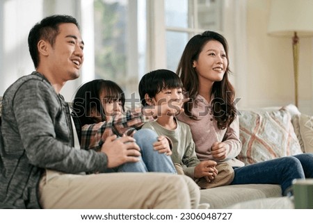 happy asian family with two children sitting on couch at home watching tv together Royalty-Free Stock Photo #2306048727