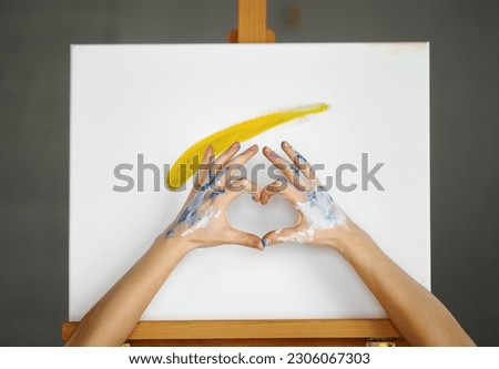 Composition of artist hands making heart shape sign over picture canvas