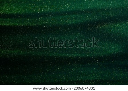 Green liquid with tints of golden glitters. Dark atmospheric background with a scattering of gold sparkles. Magic Galaxy of golden dust particles in dark green fluid.