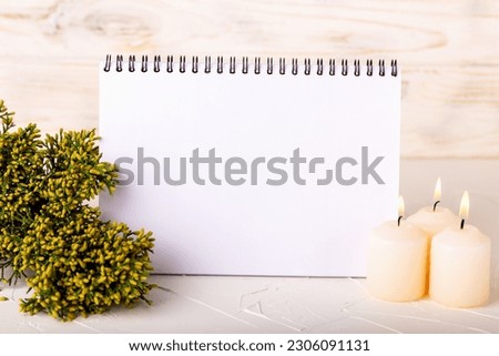 Blank notebook with juniper branch and burning candles on light background. Perfect mockup for your best design. Horizontal placement