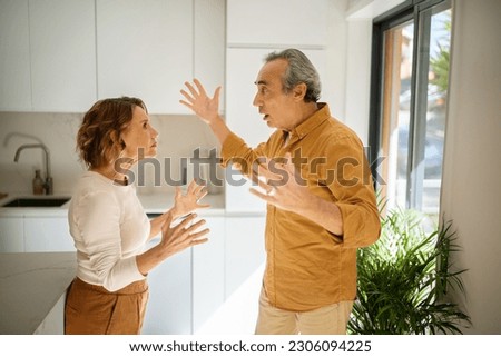 Relationship problems. Angry senior man arguing with his wife at kitchen, mad spouses shouting at each other and gesturing, having difficulties in marriage, side view Royalty-Free Stock Photo #2306094225