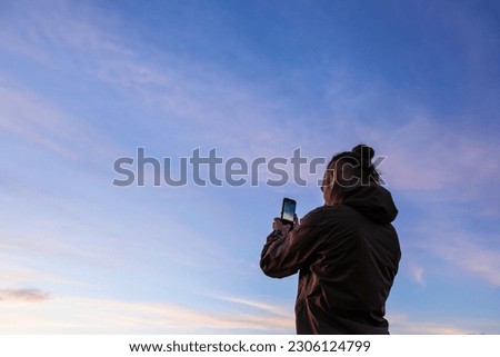 long-haired man taking mobile phone pictures of the sunset with purple, purple, orange, and blue colors