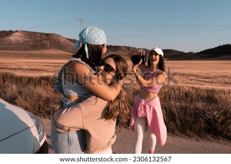 The friends hug and smile as they play on a summer afternoon and their friend takes a picture of them with her reflex camera.