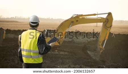 Engineer in a helmet with a digital tablet next to construction excavator	 Royalty-Free Stock Photo #2306132657