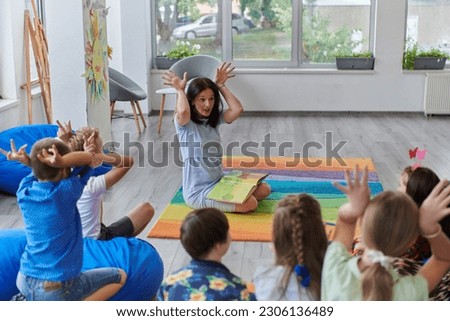 A happy female teacher sitting and playing hand games with a group of little schoolchildren Royalty-Free Stock Photo #2306136489