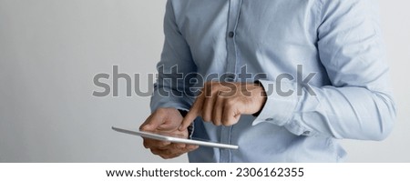 Closeup portrait of smiling young handsome man looking at camera, holding tablet computer and using it. Technology concept. Isolated view on grey background.