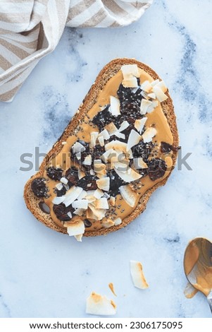 Vegan breakfast toast with peanut butter, coconut, berry and chia seeds on a white marble background.