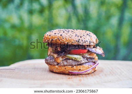 Close up picture of really juicy and tasty homemade hamburger or on the wooden plate outdoor, made from sesame seed bun, melted beef from organic farming, pickles, caramelized onion and red tomatoes.