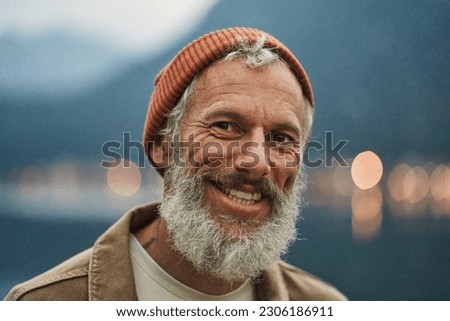 Happy older bearded man standing in nature park outdoors and laughing. Smiling active mature senior traveler looking at camera advertising camping tourism. Close up face front portrait. Royalty-Free Stock Photo #2306186911