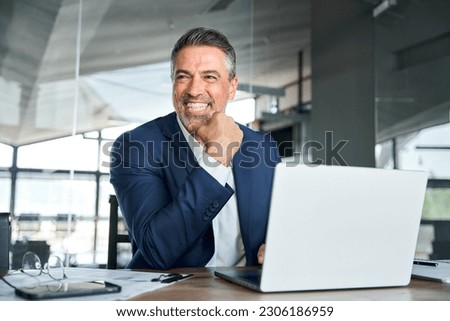Happy smiling middle aged professional business man company executive ceo manager wearing suit sitting at desk in office working on laptop computer laughing at workplace. Authentic candid photo. Royalty-Free Stock Photo #2306186959