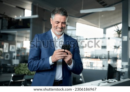 Happy middle-aged business man ceo wearing blue suit standing in office using cell phone. Older businessman professional executive holding mobile satisfied with enterprise solution management service. Royalty-Free Stock Photo #2306186967