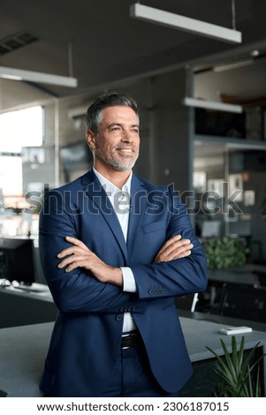 Happy proud prosperous mid aged mature professional business man ceo executive wearing suit standing in office arms crossed looking away thinking of success, leadership and growth, vertical. Royalty-Free Stock Photo #2306187015