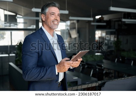 Happy middle aged business man ceo wearing suit standing in office using digital tablet. Smiling mature businessman professional executive manager looking away thinking working on fintech device. Royalty-Free Stock Photo #2306187017