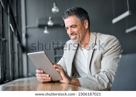 Happy mid aged business man wearing suit standing in modern office using digital tablet. Mature businessman professional manager holding tab working on financial data on fintech device. Royalty-Free Stock Photo #2306187021