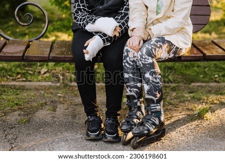 A caring mother, girlfriend, sister in roller skates holds hands in a cast of a girl, a child after a fracture from sports, motivating after rehabilitation, sitting on a bench. Photography, portrait.