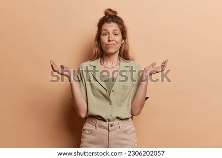 I have no idea. Clueless doubtful young European woman shrugs shoulders and looks questioned or careless dressed in fashionable clothes isolated over brown background. Whats happening I wonder Royalty-Free Stock Photo #2306202057