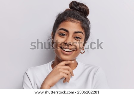Portrait of tender charming woman touches chin gently smiles broadly has healthy skin being in good mood glad to pose for making photo isolated over white background. Happy human emotions concept