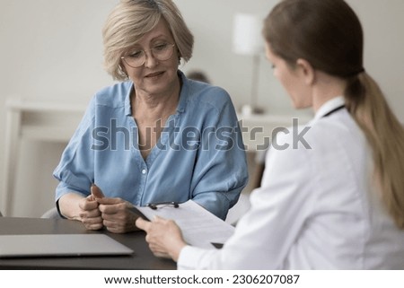 GP in white coat talk to patient seated at desk, provide professional consultation to elderly woman, hospital patient, tell about plan of disease treatment, tell for medications during visit in clinic Royalty-Free Stock Photo #2306207087