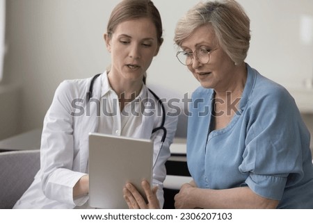 Female therapist holding digital tablet show health test check up result, share treatment plan to mature woman during visit in clinic office. Patient receive professional medical air, tech, medicine Royalty-Free Stock Photo #2306207103